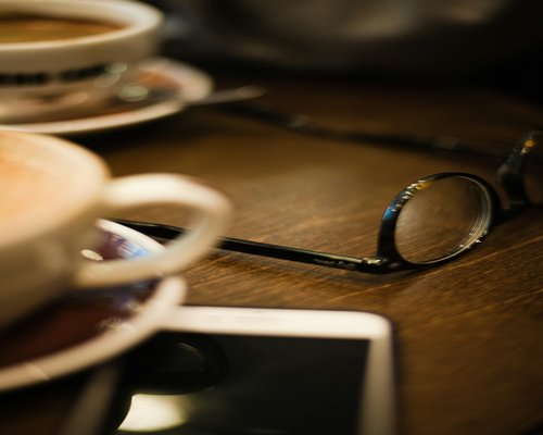 Cup of coffee next to reading glasses